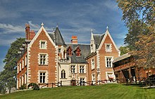 Photo of a large medieval house, built of brick with many windows and gables and a circular tower with a conical roof.