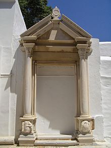 photographie couleurs : deux colonnes et un fronton de marbre posés contre un mur blanc