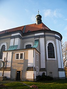 Presbytář, zřetelně viditelná okna, zdvojené pilastry, vlevo sakristie s oratoří v patře, před ní misijní kříž, ze střechy vybíhá sanktusník