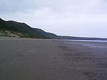 Photograph of the wide sandy beach with hills behind it