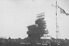 Photo en noir et blanc de l'îlot d'un porte-avions, sur lequel on distinque bien le radar