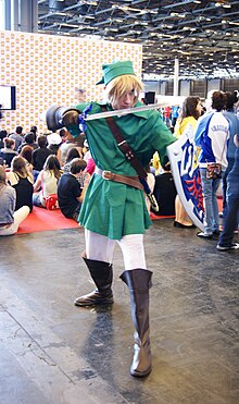 Homme habillé de vert en costume de Link, brandissant une épée et tenant un bouclier à l'autre bras.