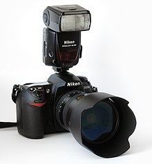 Farbfotografie einer modernen Kamera von Nikon mit einem externen Kamerablitz und einem großen Objektiv.