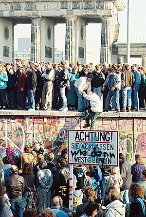 People atop the Berlin Wall near the Brandenbu...