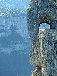 Une route à flanc de précipice passe sous une arche dans la roche.