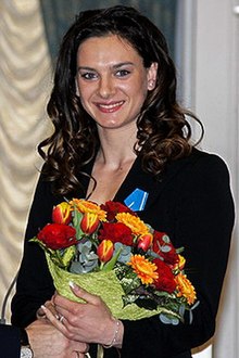 Photographie d'Isinbayeva en costume noir tenant un bouquet de fleurs jaunes et rouges