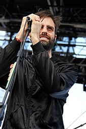 A man in a black jacket holding a microphone on stage.