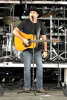 Country singer Rhett Akins, singing into a microphone and holding an acoustic guitar