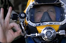 A diver touches his first finger tip to his thumb tip while extending his other fingers