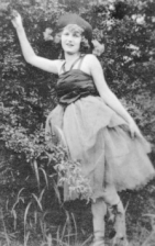 Черно-белая фотография молодой женщины на открытом воздухе в балетной позе с вытянутой рукой. Она смотрит в камеру.