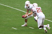 In a hand-off, the quarterback (wearing #12 in this photo) can hand the ball to the running back (#25)