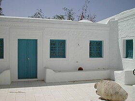 Cour intérieure d'un houch avec ses murs blancs, sa porte et ses grilles aux fenêtres de couleur bleue.