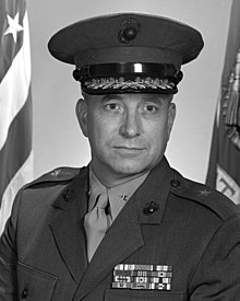 A grayscale photo of a white man in a US Marine Corps uniform (with single stars on the epaulets; he is weating a cap and looking slightly to the camera's right.