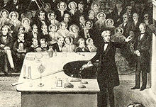 Michael Faraday, nineteenth century scientist and electrician, shown delivering the British Royal Institution's Christmas Lecture for Juveniles during the Institution's Christmas break in 1856. Faraday xmas detail.jpg