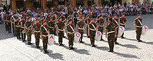 Uniformed band members standing in formation, the band leader in front.