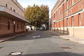 One-way street towards camera turning right, surrounded by parking and two-storey buildings on both sides