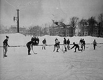 A group of men skate on ice in two groups, each trying to hit a small rubber disc with curved sticks