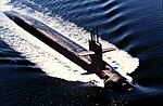 Aerial view of submarine running on surface; antennas are raised from the boat's sail.