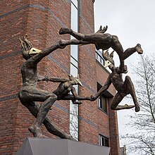 A metal sculpture of four dancers in pointed masks, holding hands and spinning wildly