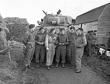 Photo en noir et blanc d'un groupe de soldats en tenue de combat se tenant devant un char d'assaut