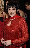 A woman in a red dress, jacket and scarf smiles toward the camera.