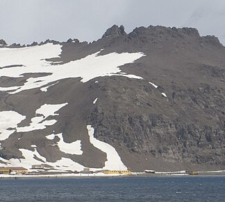 Blick von der Admiralty Bay auf das Kliff Krzesanica mit dem östlichen Teil des Panorama Ridge (Hintergrund) und der davorliegenden Arctowski-Station