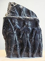 Prisoners escorted by a soldier, on a victory stele of Sargon of Akkad, circa 2300 BCE.[۱۸] The hairstyle of the prisoners (curly hair on top and short hair on the sides) is characteristic of Sumerians, as also seen on the Standard of Ur.[۱۹] Louvre Museum.