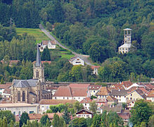 Vue du centre de Ronchamp et de son église derrière lesquels se trouvent une colline boisée d'où émerge le chevalement.