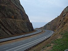 A highway passes through a cut through a mountain. The rock walls of the cut are visible above the highway.