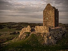 Ruines d'une haute maison de pierres sur un rebord rocheux.