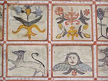 Photo en couleur de quatre carrés peints, deux avec des fleurs et des arabesques, et en dessous, l'un avec un long animal rayé, l'autre avec une tête humaine sur des ailes