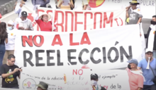 Street protestors holding a white banner with red text reading "No to Re-Election" in Spanish.
