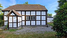 A view of the black and white timber frame building with a small porch; gravel on the ground around; blue sky