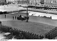 Photo d'archive en noir et blanc de la place de la Gare, montrant des soldats allemands formant un carré autour de gradés.