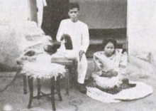 Woman weaving buntal hats while a man is using a charcoal iron to shape finished hats (c.1929) Buntal hat weaving (1929).png