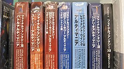 Seven thick large paperback books, each with different Japanese writing on the binding, wrapped in plastic, sitting on a shelf in a row
