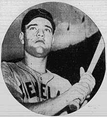 A man in a light baseball jersey with "Cleveland" written across the chest and a dark cap