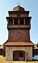 Ein mächtiger, etwas gedrungener Holzturm auf einem Steinfundament, in das das Eingangstor zur Kirche eingelassen ist