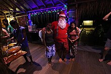 A man dressed as Santa hugging two women in a small night club