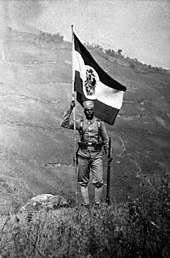 An East African Askari soldier holding Germany's colonial flag Bundesarchiv Bild 105-DOA6369, Deutsch-Ostafrika, Askari.jpg