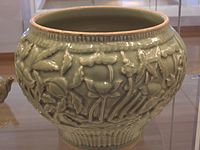 A celadon shoulder pot from the late Yuan dynasty, displaying artwork of peaches, lotuses, peonies, willows, and palms