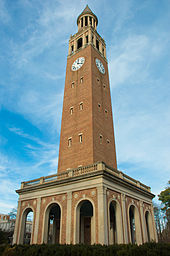 A bell tower in the night with lit up archways at the base and a clock near the top of the tower.