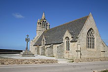 À gauche, le calvaire. Au fond, le clocher-mur avec ses deux tourelles. La façade sud, avec grands contreforts, est percée de deux baies. Au premier plan, le chevet, percé d'une grande baie, est prolongé par le pignon de la remise.