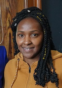 Porträt einer jungen schwarzen Frau, die offen lächelnd in die Kamera blickt.