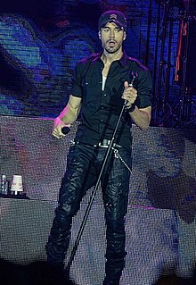 A man wearing a black cap, shirt, and pants is holding a microphone stand on its left side