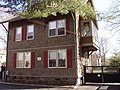 A brown 2 1/2 story house with red shutters.