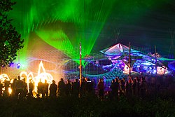 Festival attendees stand silhouetted against a multicoloured laser-light show