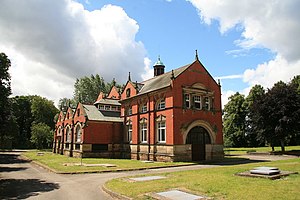 Ornate Edwardian red brick building with high facade surrounded by lawns on a sunny dat against a blue sky with white clouds