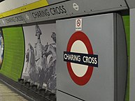 A platform wall: a panel contains the London Underground roundel with "CHARING CROSS" in the centre. A band contains the station name along the top of the wall. A decorative panel shows a photo-montage of Lord Nelson from the top of Nelson's column and the lions from around its base