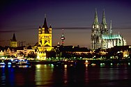 Cologne skyline at night with river Rhine in the foreground and famous Cologne Cathedral on the right. The towers of Town Hall (on the left) and Great St. Martin church (centre) are visible as well.